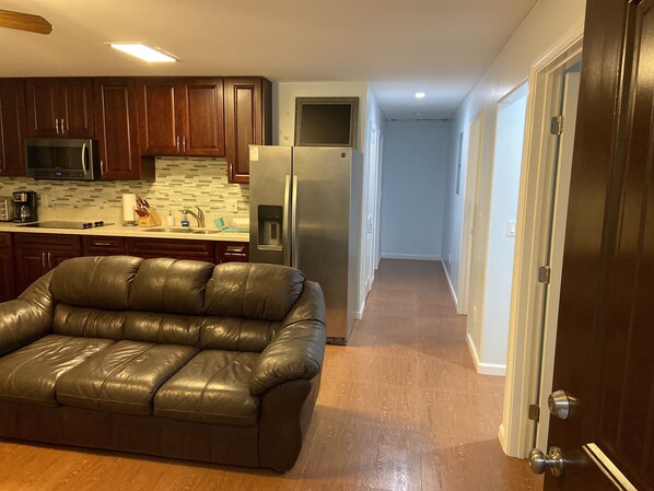 A modern kitchen with dark wooden cabinets, stainless steel appliances, and a leather sofa in the living area.