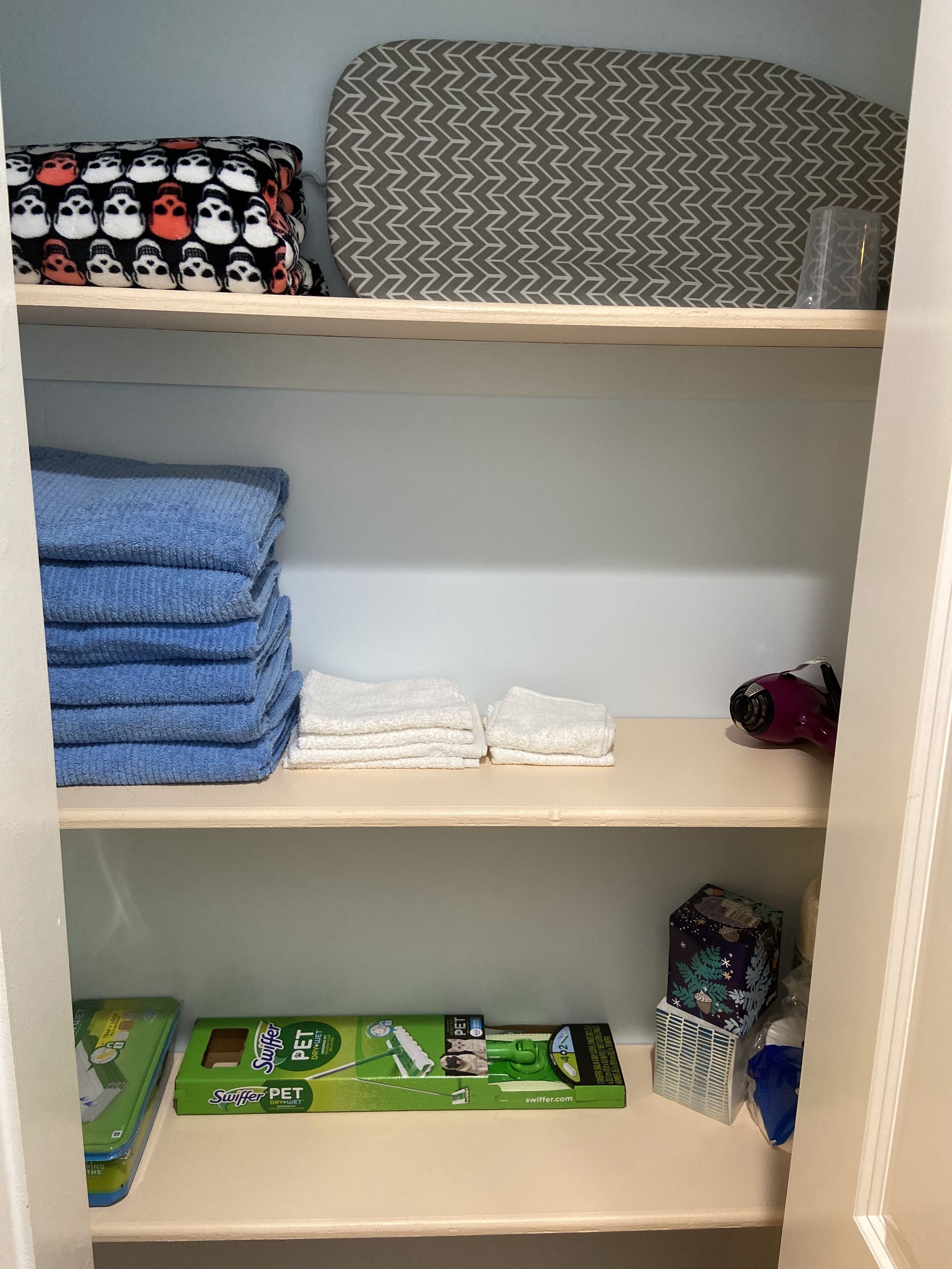 Um espaço de armazenamento com prateleiras contendo toalhas dobradas, uma cama para animais de estimação, um secador de cabelo e produtos para animais.