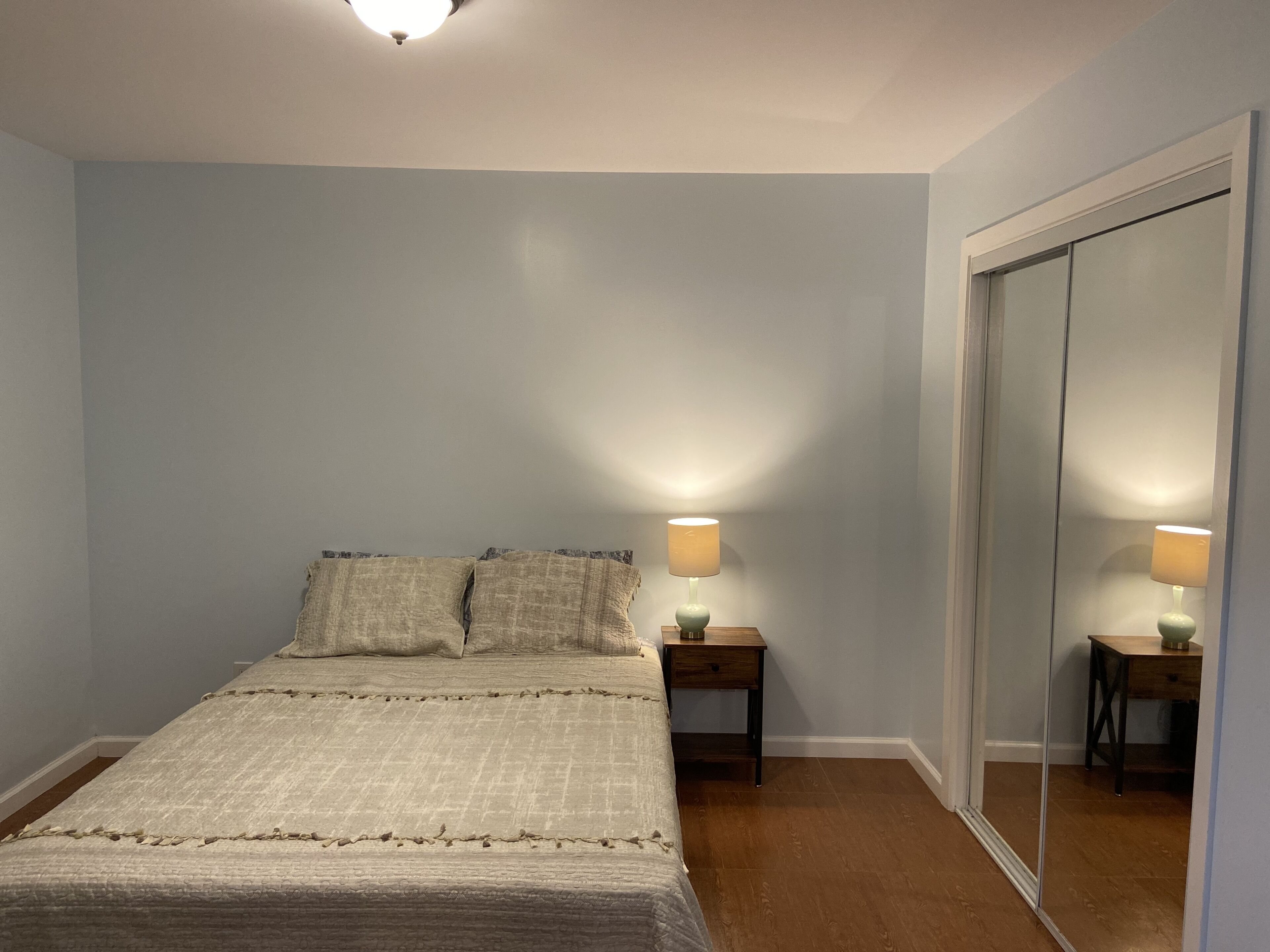 Een slaapkamer met een bed, twee nachtkastjes met lampen, een kledingkast en een plafondlamp.