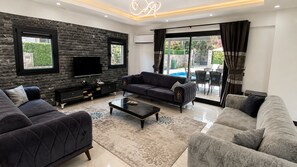 A modern living room with a sofa set, a coffee table, and a flat-screen TV mounted on a stone wall. - Villa Kayahan Göcek (Fethiye)
