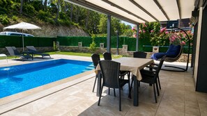 Ein überdachter Außenbereich mit Pool, Sitzgelegenheiten und einem Tisch.