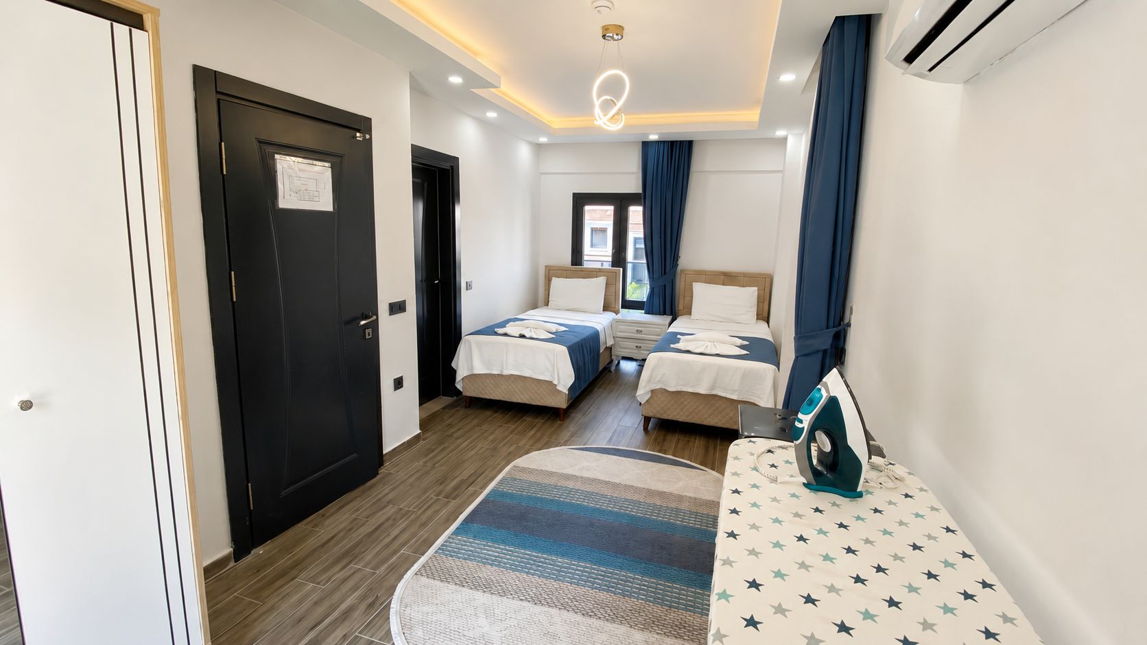 Et hotelværelse med to senge, en rund måtte, strygebræt og en aircondition.