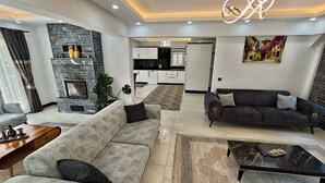 A modern living room with a fireplace, sofas, a coffee table, and a kitchen in the background. - Villa Kayahan Göcek (Fethiye)