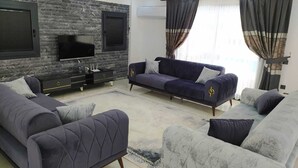 A modern living room with a stone wall, a flat-screen TV, a dark blue sofa, and a patterned rug. - Villa Kayahan Göcek (Fethiye)