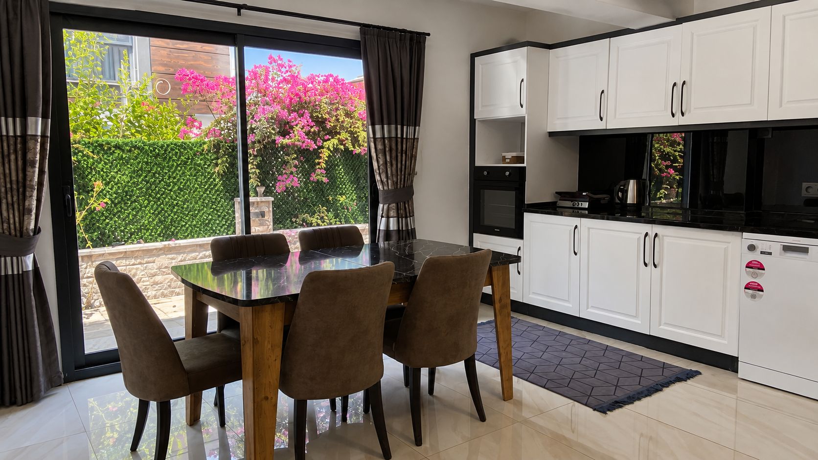 Une cuisine moderne avec des meubles blancs, un plan de travail noir et un coin repas comprenant une table et des chaises en verre.