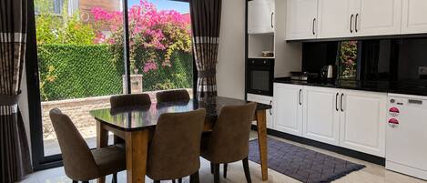 Een moderne keuken met witte kasten, een zwart aanrechtblad en een eethoek met een glazen tafel en stoelen.