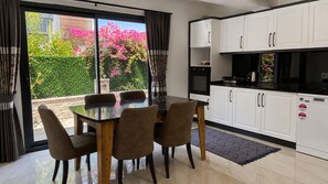 A modern kitchen with white cabinets, a black countertop, and a dining area with a glass table and chairs. - Villa Kayahan Göcek (Fethiye)
