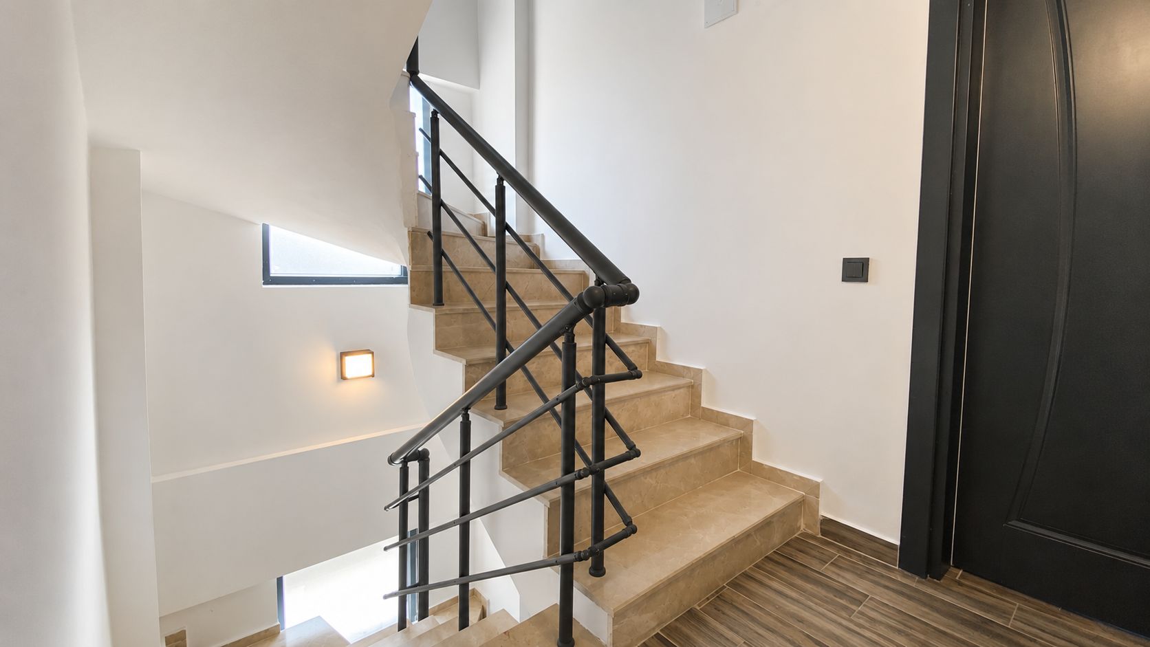 Eine Treppe mit schwarzem Metallgeländer, die zu einer Zwischenebene führt.