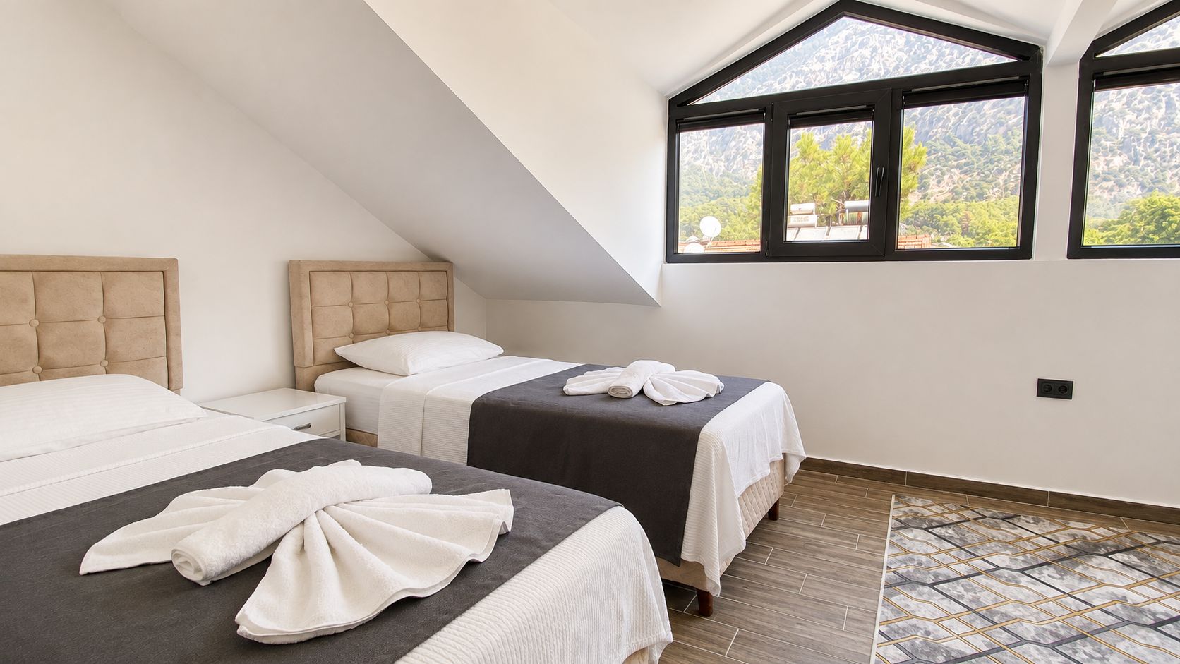 A hotel room with two beds, a large window with a mountain view, and a modern design.