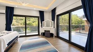 A bedroom with a bed, a vanity, and large windows. - Villa Kayahan Göcek (Fethiye)