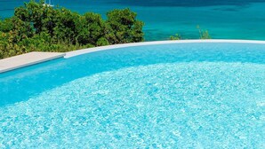 Una piscina infinita azul cristalina con vistas al océano y barcos.
