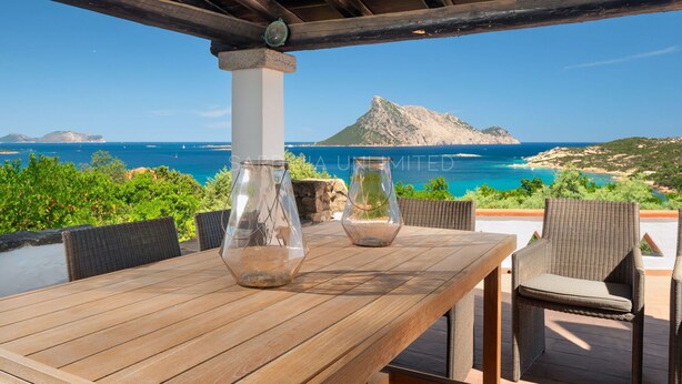 Una mesa de madera con dos jarrones de vidrio, sillas de mimbre y vistas al mar y a las montañas.