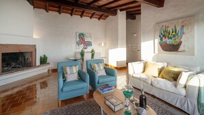 Una sala de estar con chimenea, dos sillones azules, un sofá blanco y una pintura de un cactus.