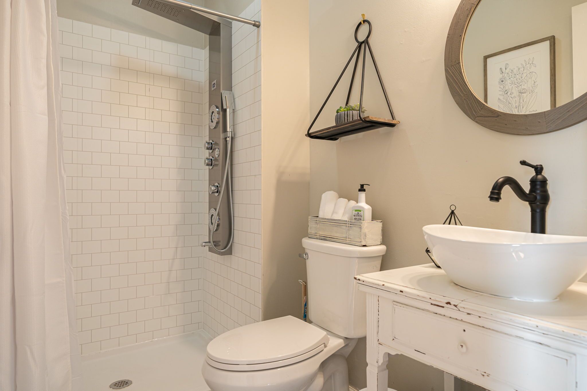 Een badkamer met een witte betegelde douche, een toilet, een wastafel met een groot bassin en een hangplank met toiletartikelen.