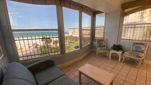 Un balcone con divano, sedie e tavolo, con vista sulla spiaggia e sugli edifici.