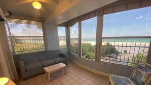Un balcone con un divano, un tavolino e una sedia, con vista sulla spiaggia.