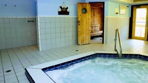 Una stanza spa con vasca idromassaggio, pareti in piastrelle e porta in legno per la sauna.
