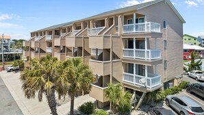 Un hotel de varios pisos con balcones, zona de estacionamiento y palmeras.