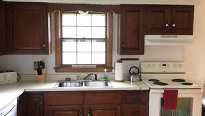 A compact kitchen with wooden cabinets, a white stove, and a window above the sink.