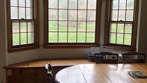 A dining area with a wooden table and chairs, large windows with a view of a grassy yard, and a built-in bench with storage.