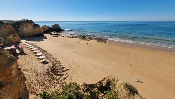 A beach with a clear sky, rocky cliffs, and a sandy shore.