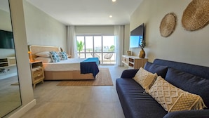 A modern hotel room with a large bed, a dark sofa, and a TV on the wall.