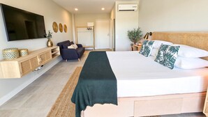 A modern bedroom with a large bed, a TV mounted on the wall, a sofa, and a small table with a plant.