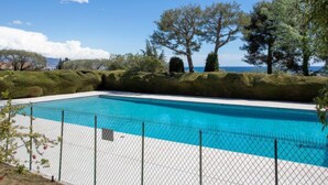 En rektangulær swimmingpool med krystalklart, blåt vand, omgivet af en hvid flisegang og et hegn af metalnet.