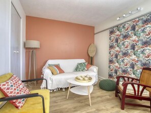 Uma sala de estar aconchegante com um sofá, uma mesinha redonda com uma bandeja de xícaras, um abajur e uma cortina estampada.