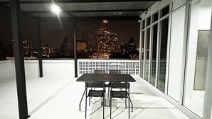 Una terrassa exterior amb taula i caires, vista d'un paisatge urbà de nit, i una partició de vidre.