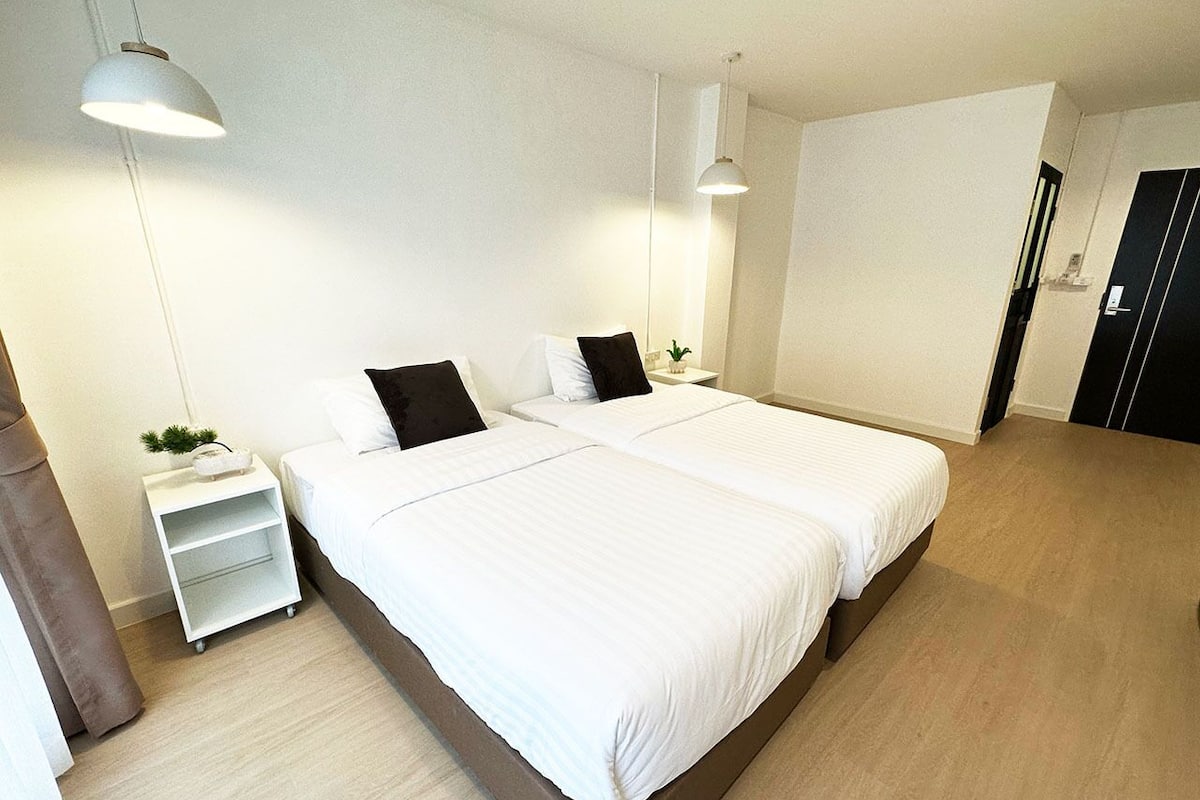 Una habitación de hotel moderna con dos camas, una mesita de noche pequeña con una planta y un armario.