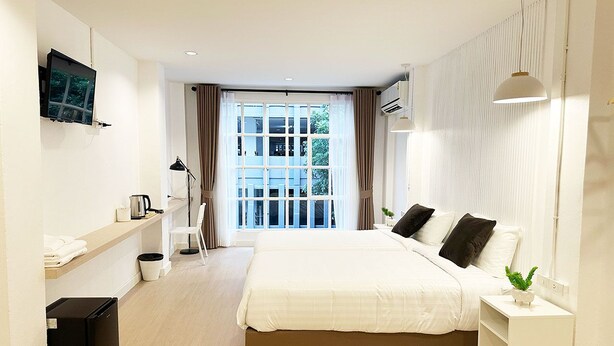 Habitació d'hotel moderna amb un llit gran, una televisió penjada a la paret, una cuineta petita i vista cap a l'exterior per la finestra.