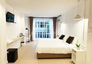 A modern hotel room with a large bed, a TV mounted on the wall, a small kitchenette, and a view of the outdoors through the window. - River Home (Bangkok)