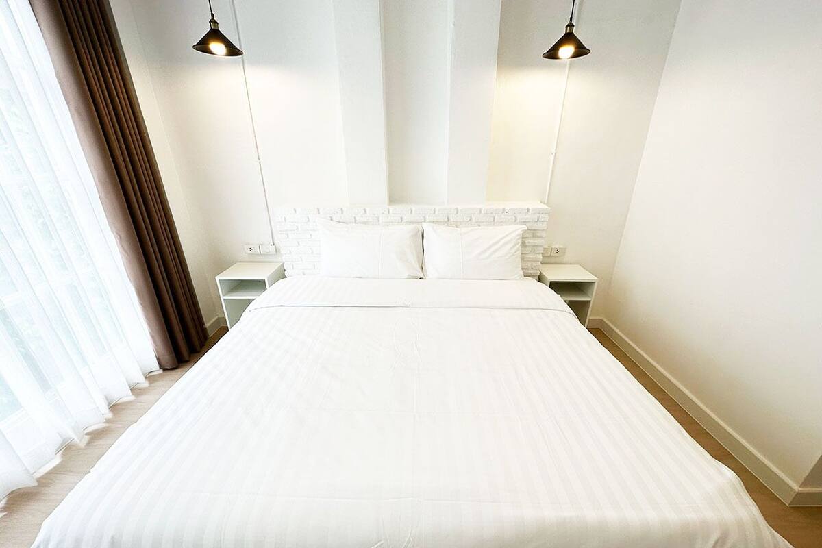 Una cama grande con ropa blanca, dos mesitas de noche y dos lámparas colgantes.