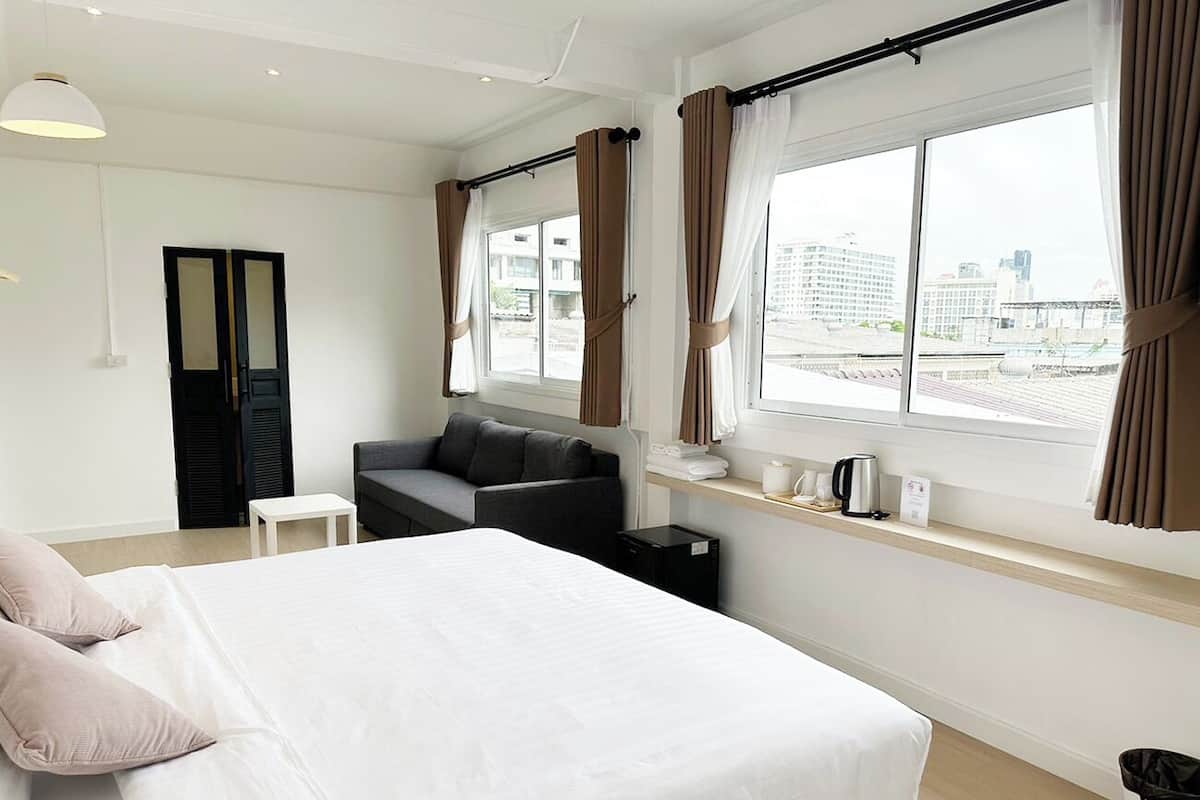 Habitación de hotel con una cama grande, un sofá, una mesita, una ventana con cortinas y vistas a la ciudad.