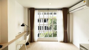 Habitació d'hotel moderna amb una finestra gran, un escriptori, una cadira i un aparell d'aire condicionat.