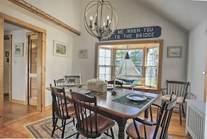 A dining area with a large wooden table, chairs, and a chandelier. There is a window with blinds and a sign above the table.