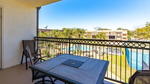 A balcony with a table and chairs, overlooking a swimming pool and buildings. - Walk-to-Beach Condo with Resort Pool (Biloxi)
