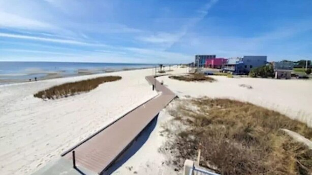 A beach with a pathway leading to a building with a flat roof and a pink section. - Walk-to-Beach Condo with Resort Pool (Biloxi)