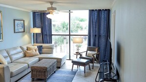 A living room with a sofa, armchair, and ottoman, a television, and a ceiling fan. - Walk-to-Beach Condo with Resort Pool (Biloxi)