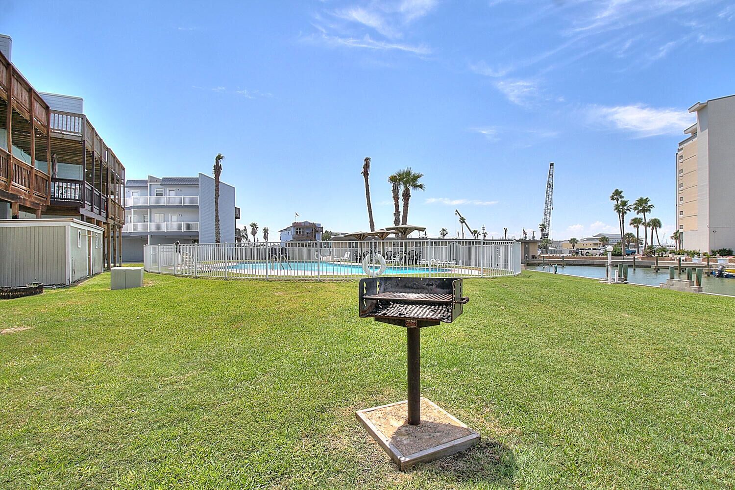 A grassy outdoor area with a barbecue grill, a swimming pool, and a white fence.