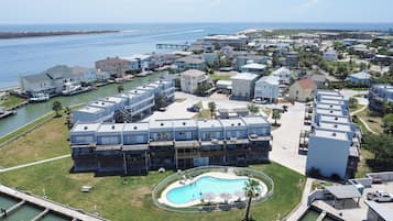 A coastal residential area with a large swimming pool surrounded by a fence, multiple-story buildings, and a marina with boats.