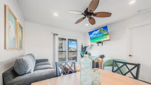 A modern living room with a grey sofa, a wooden dining table, and a ceiling fan. - With the best amenities in Port Aransas! Large swimming pool, private lighted fi (Port Aransas)