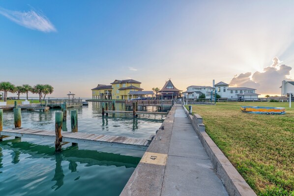 Propiedad frente al agua con muelle, zona verde y edificios de diversos estilos arquitectónicos.