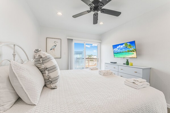 A bedroom with a bed, pillows, a ceiling fan, a television, and a window with a view of the outdoors.