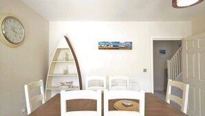 A dining area with a wooden table, white chairs, a clock, and a shelf with decorative items. - Light, modern townhouse with patio, a minute from beach; child- and pet-friendly (Goring-by-Sea)