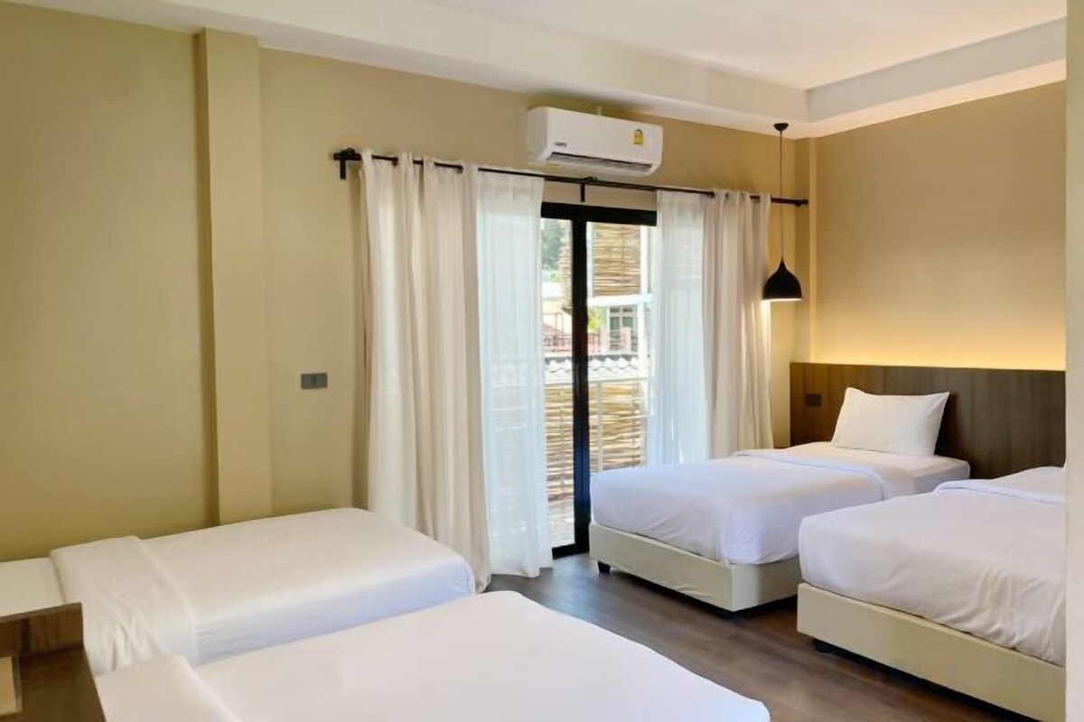 A hotel room with two beds, a balcony with curtains, and an air conditioning unit.