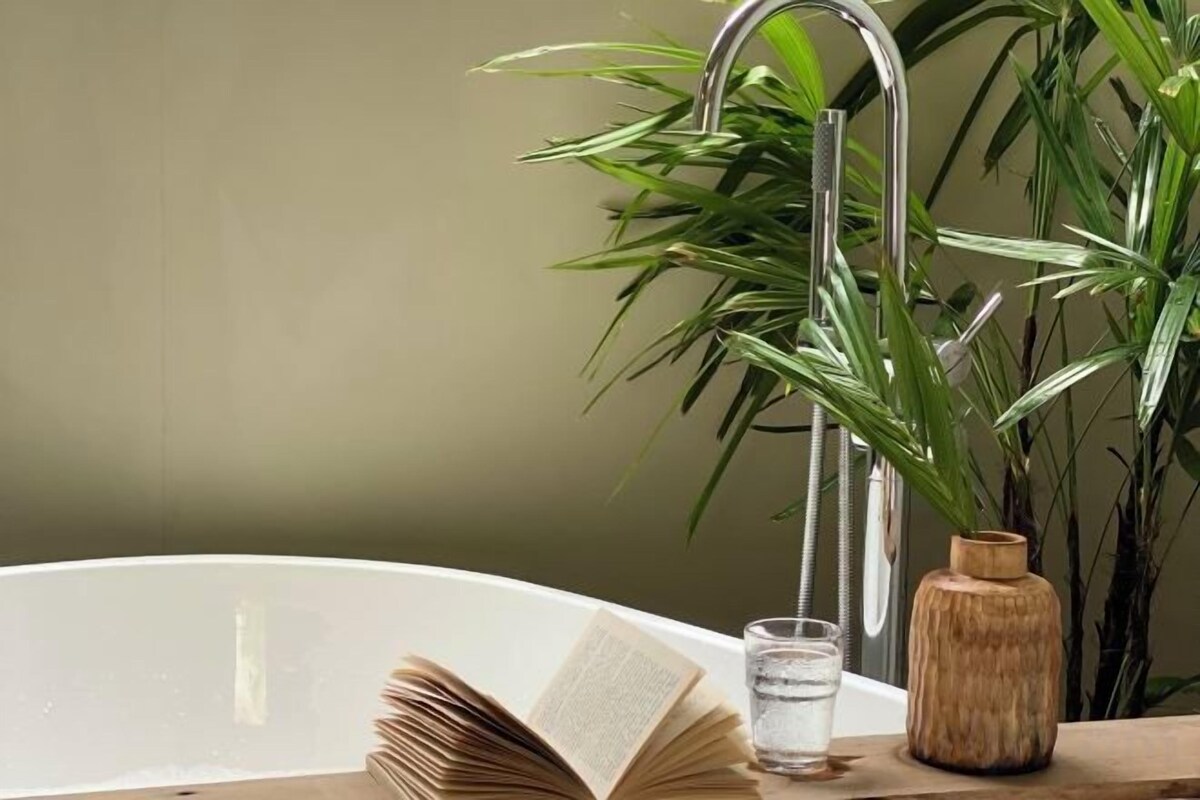 A bathtub with a book, a glass of water, and a wooden vase.