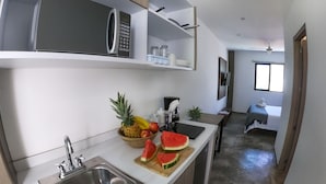 Une cuisine moderne équipée d’un four à micro-ondes encastré, d’un évier et d’un plan de travail sur lequel sont disposés des fruits. On y trouve également un petit coin repas avec une table et une chaise.