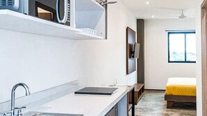 Une cuisine moderne équipée d’un four à micro-ondes encastré, d’un évier et d’un plan de travail. La pièce adjacente contient un lit recouvert d’une couverture jaune.